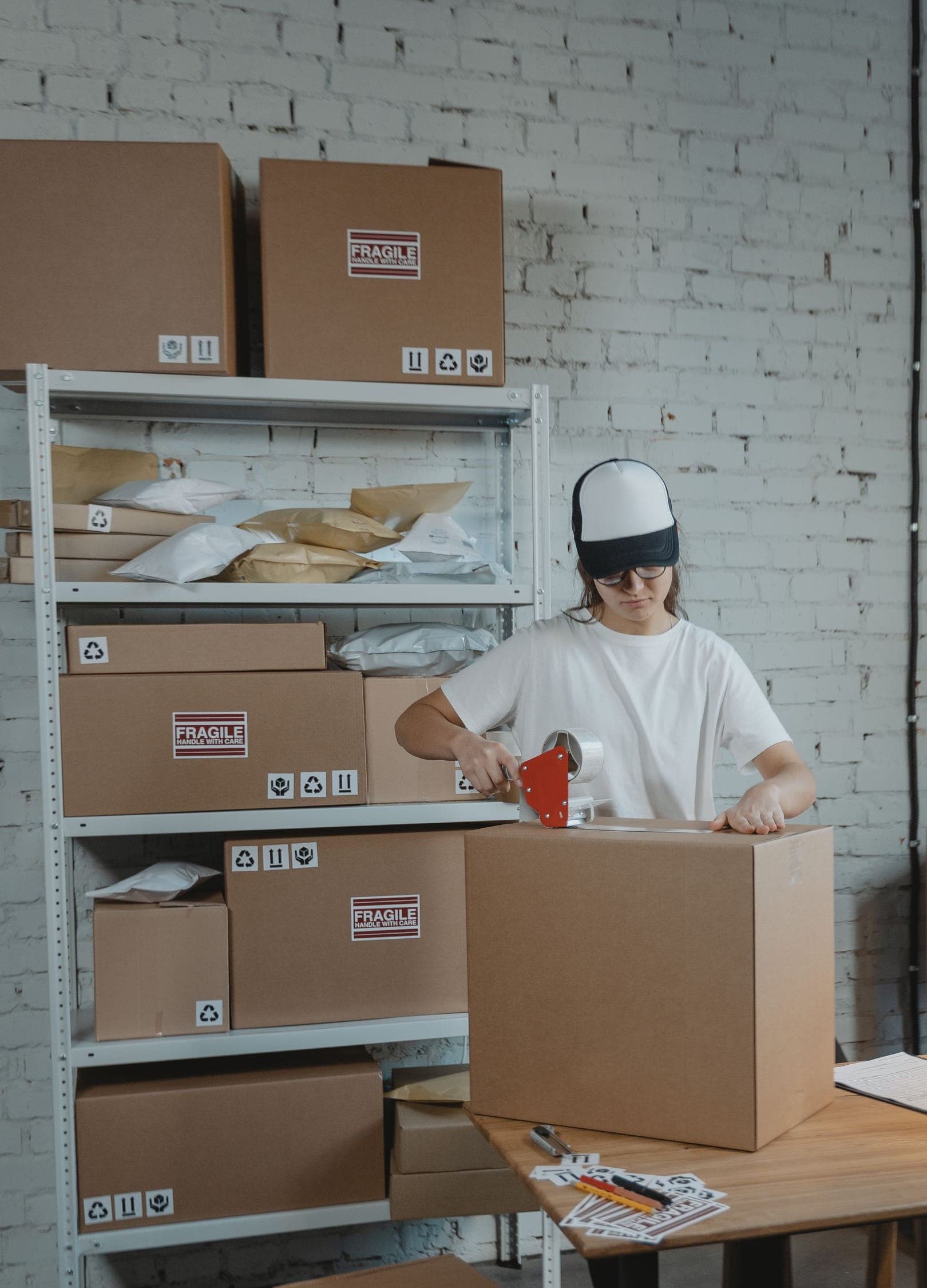 A worker sealing a carton at a packing table, with labeled boxes on the shelves behind the station.